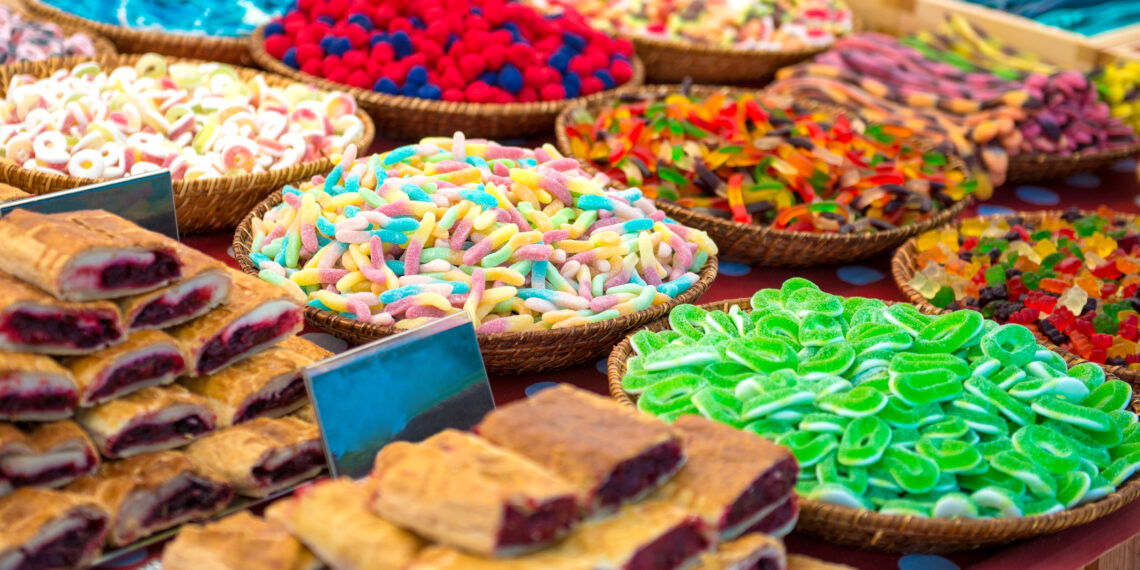 Colourful baskets of assorted festival sweets and pastries displayed at a vibrant market stall, including gummy candies, sugar-coated treats, and fruit-filled pastries reminiscent of Caribbean Carnival sweet snacks.