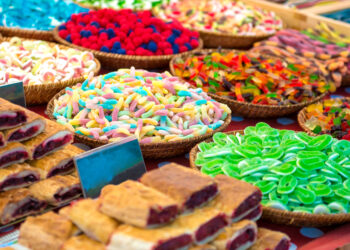 Colourful baskets of assorted festival sweets and pastries displayed at a vibrant market stall, including gummy candies, sugar-coated treats, and fruit-filled pastries reminiscent of Caribbean Carnival sweet snacks.