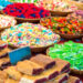 Colourful baskets of assorted festival sweets and pastries displayed at a vibrant market stall, including gummy candies, sugar-coated treats, and fruit-filled pastries reminiscent of Caribbean Carnival sweet snacks.