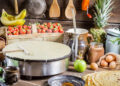 Various roti-making equipment including a tawa pan, cast iron griddle, belna rolling pin, and roti press arranged on a kitchen countertop, ready for preparing fresh rotis at home.
