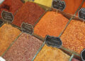 Assorted colourful ground spices and chilli flakes displayed in open bins at a market spice shop