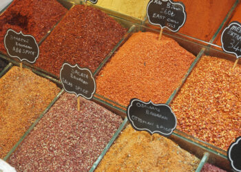 Assorted colourful ground spices and chilli flakes displayed in open bins at a market spice shop