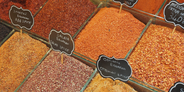 Assorted colourful ground spices and chilli flakes displayed in open bins at a market spice shop