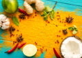 Colourful Caribbean spice spread with turmeric powder, ginger, garlic, lime, chillies, star anise, mint, and coconut on a blue wooden surface