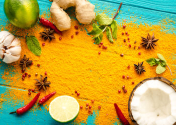 Colourful Caribbean spice spread with turmeric powder, ginger, garlic, lime, chillies, star anise, mint, and coconut on a blue wooden surface