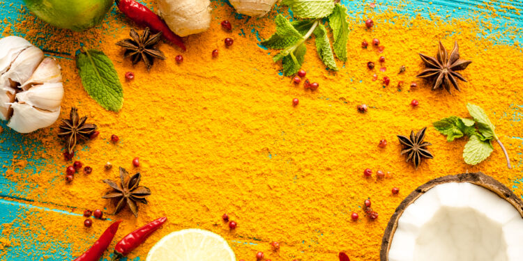 Colourful Caribbean spice spread with turmeric powder, ginger, garlic, lime, chillies, star anise, mint, and coconut on a blue wooden surface