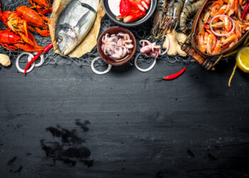 Fresh Caribbean seafood including shrimp, crab, fish, and lobster arranged with chilli and lemon on a dark surface