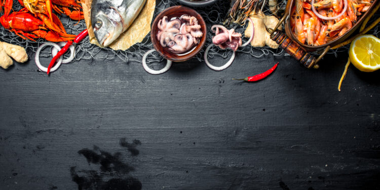 Fresh Caribbean seafood including shrimp, crab, fish, and lobster arranged with chilli and lemon on a dark surface