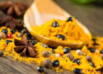 Indo-Caribbean curry powder with whole spices like peppercorns and star anise on a wooden spoon