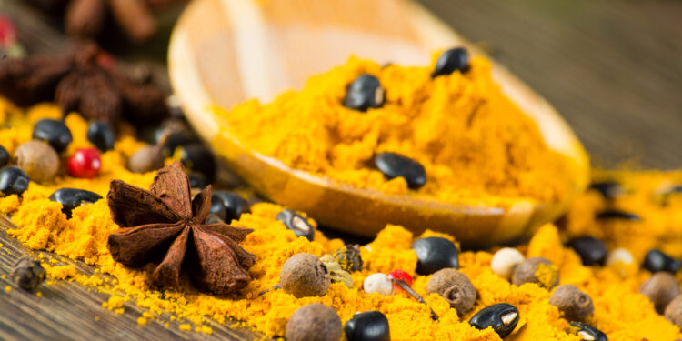 Indo-Caribbean curry powder with whole spices like peppercorns and star anise on a wooden spoon