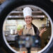 Young home cook filming a recipe video through a ring light while holding fresh vegetables in a modern kitchen.