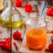 Jar of homemade Caribbean pepper sauce made with red chillies and habanero peppers on a rustic wooden table, surrounded by fresh peppers, garlic, lemon, and oil.