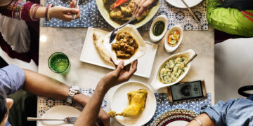 Friends sharing multicultural dishes with curry, roti, rice and sauces representing hybrid cuisine trends